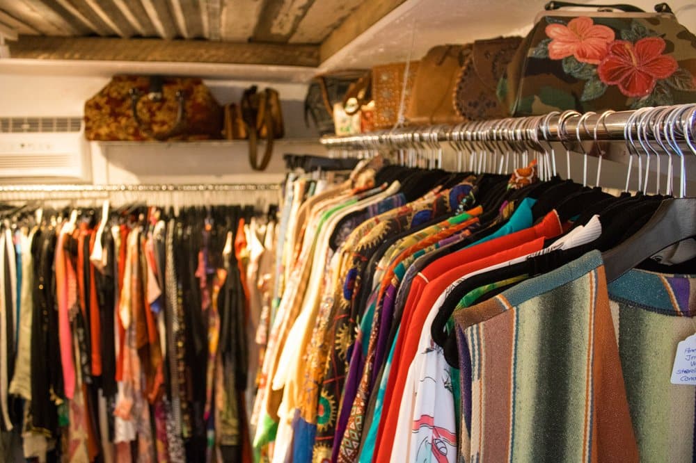 Vintage clothing items displayed on hangers in a shop with purses and accessories on a shelf above.