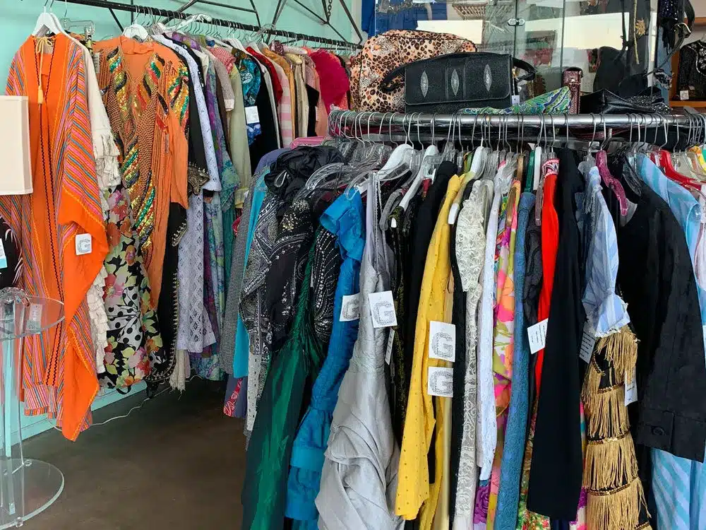 An assortment of colorful garments hanging on racks in a clothing store with price tags visible, indicating a retail or thrift store environment.