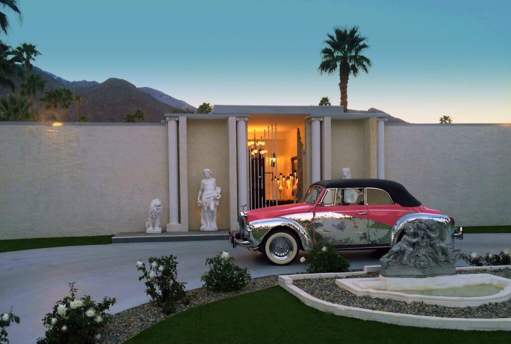 Classic car parked in front of upscale home with sculptures