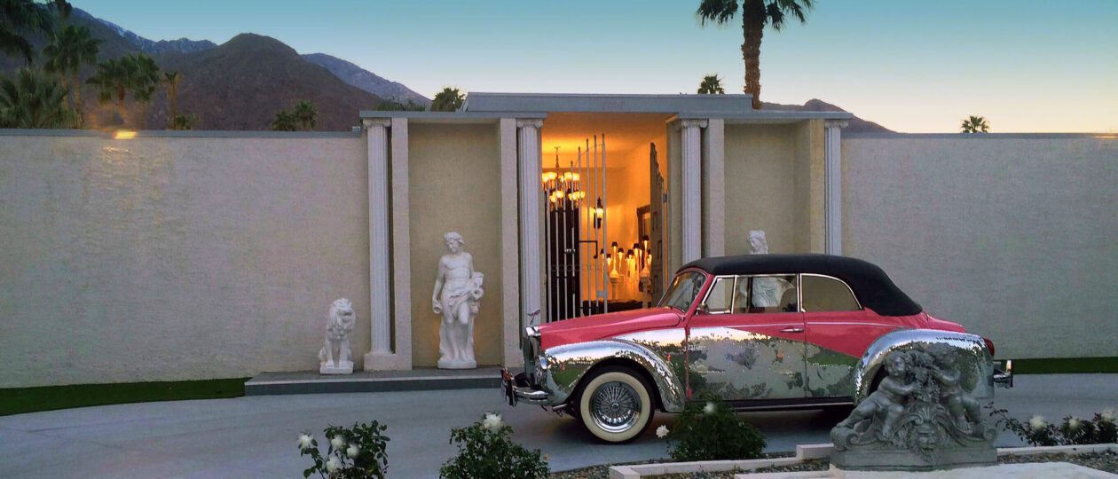Classic car parked in front of upscale home with sculptures