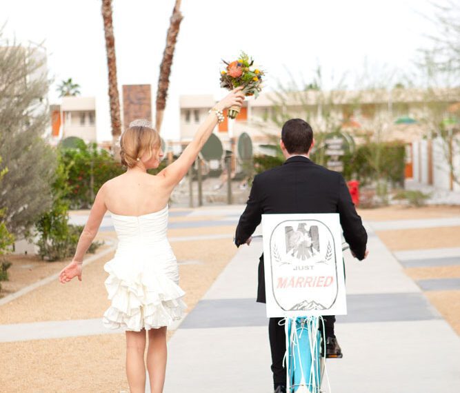 groom on bike and bride walking beside him