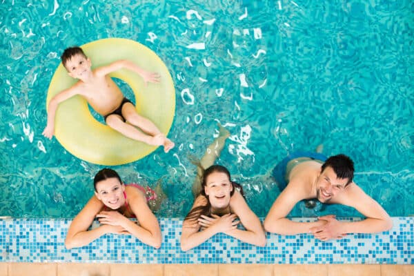 Happy family relaxing at the edge of the swimming pool, little boy relaxing on inflatable ring.