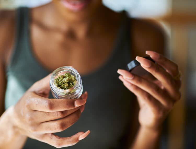 african american woman opening bottle of legal marijuana from dispensary close up with selective focus on weed