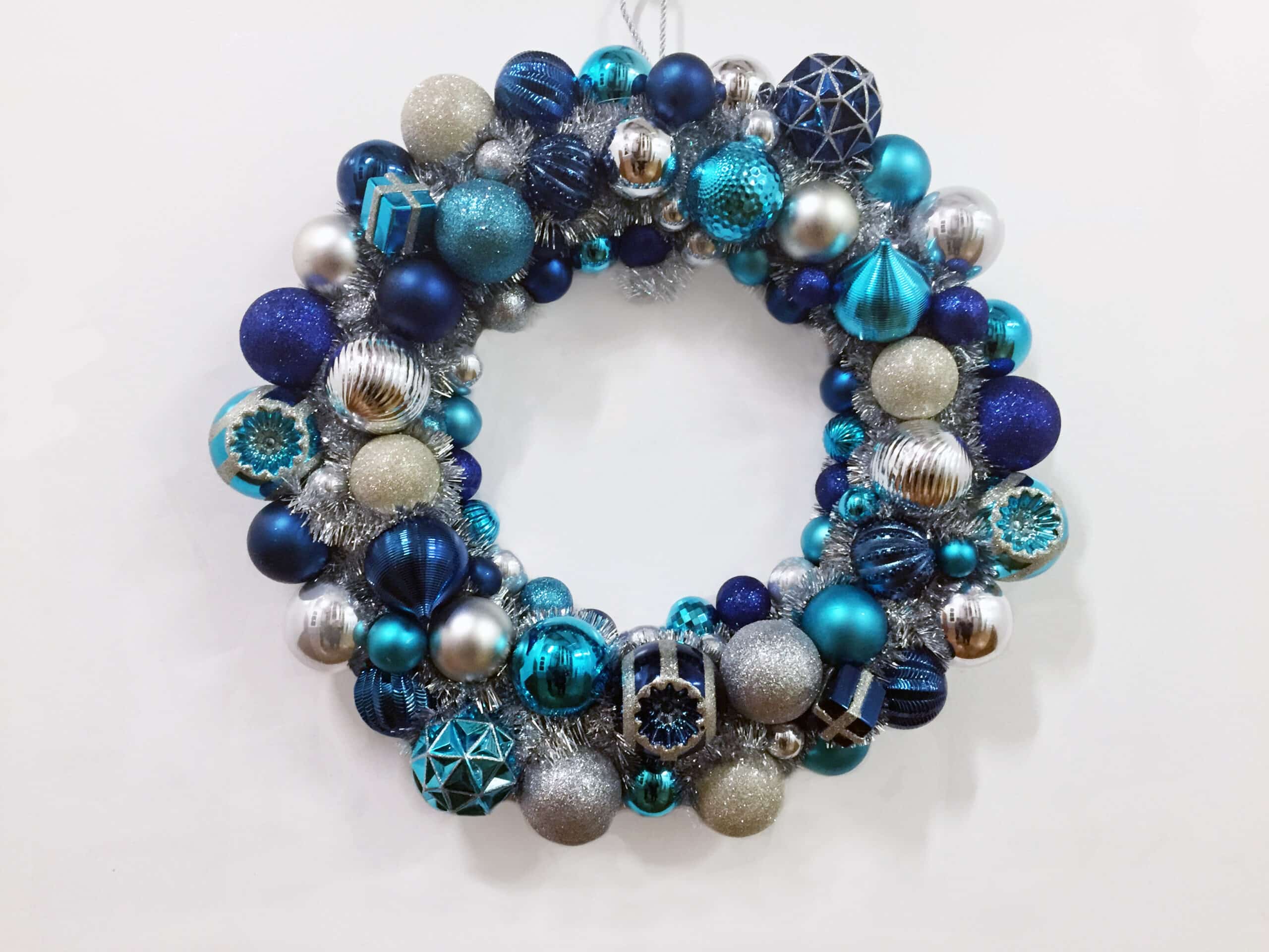 Beautiful blue wreath for Christmas decoration is made from blue and sliver balls and hung on a white wall.