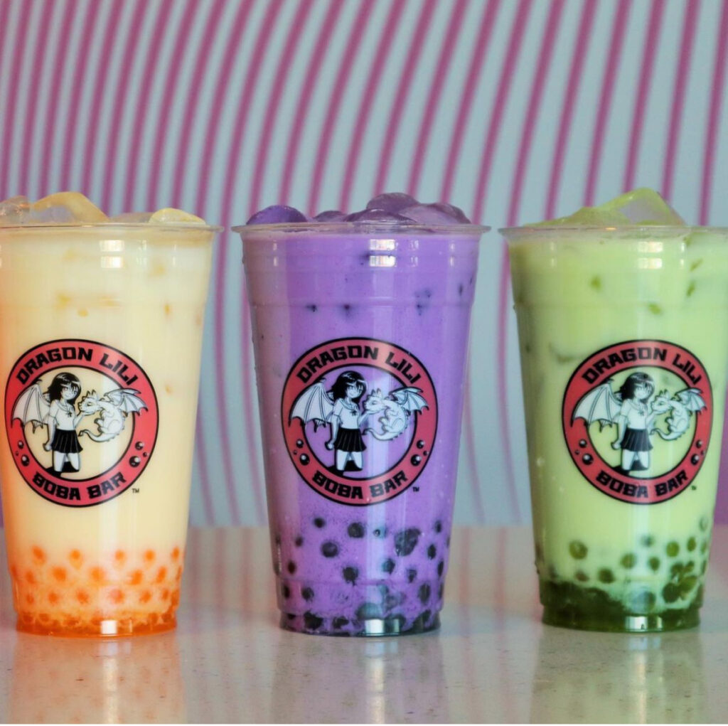 Three colorful bubble tea drinks from Dragon Lily Boba Bar, each featuring tapioca pearls, in clear cups with the shop's logo on them.