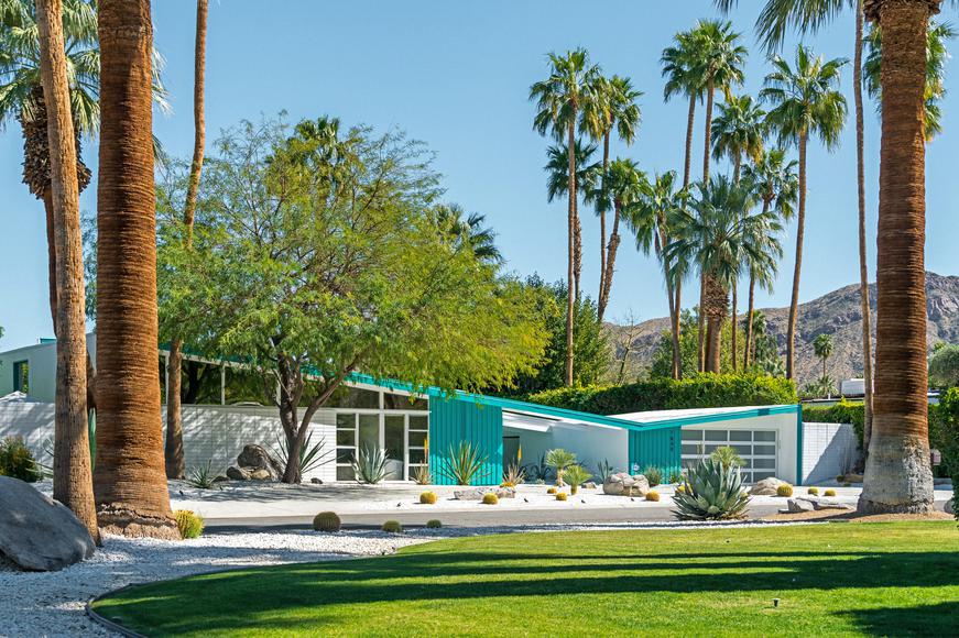A modern mid-century house with turquoise accents surrounded by palm trees under a clear blue sky.