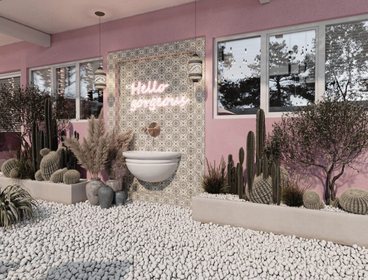 A cozy outdoor corner with a bohemian vibe featuring a neon "Hello gorgeous" sign above a white wall-mounted basin amidst decorative elements like potted cacti, pebbles, dried pampas grass, and ornate Moroccan lanterns, all set against a pink-walled backdrop with large windows showing reflections of outdoor scenery.